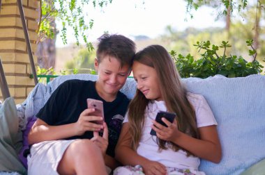 boys and a girl are sitting on the terrace with phones and playing