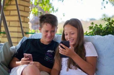 boys and a girl are sitting on the terrace with phones and playing