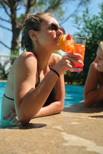 a pretty young girl in a bikini at a swimming pool with a cocktail in her hand
