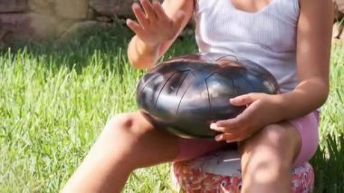 Bahçede bir kız meditasyon yapıyor ve dil davulu çalıyor.