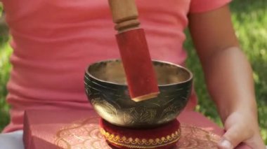 Bir kız elinde Tibet kâsesiyle bahçede çimlerin üzerinde oturuyor.