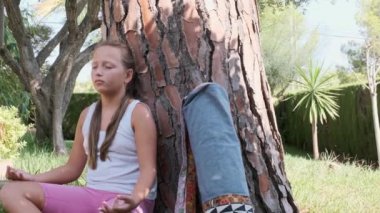 Bir kız ağaçların altındaki bahçede meditasyon yapıyor.