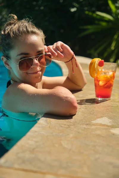 a pretty young girl in a bikini at a swimming pool with a cocktail in her hand