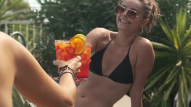 Yüzme havuzunda elinde kokteyllerle bikinili iki güzel kız.