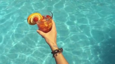 Kız havuz suyunun üzerine uzanmış kolunda bir kokteyl tutuyor.