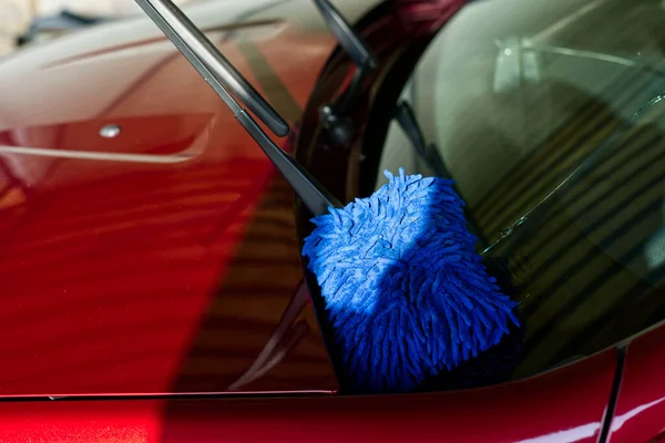 Parte de un coche rojo. Un parabrisas con capucha y una esponja para lavar son visibles — Foto de Stock