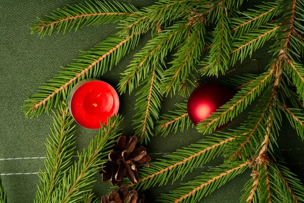 Twee takken van een kerstboom met een kerstspeeltje en een kleine rode kaars liggen op een groene doek. — Stockfoto