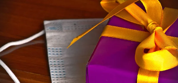 Una hermosa caja de regalo atada con una cinta de color dorado y un primer plano de máscara médica — Foto de Stock