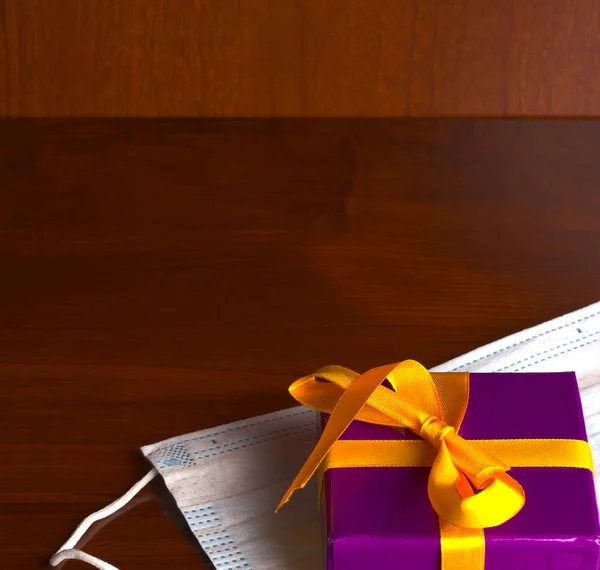 Una hermosa caja de regalo atada con una cinta de color dorado y un primer plano de máscara médica. — Foto de Stock
