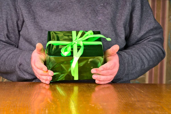 Um homem está sentado em uma mesa com um presente de aniversário verde recém-recebido — Fotografia de Stock