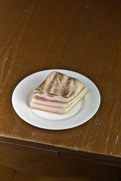 Кусок бекона со слоем красного на белой тарелке. — стоковое фото
