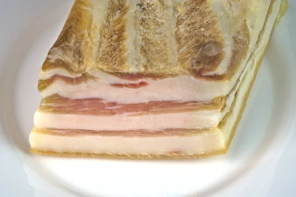 En bit bacon med ett lager rött på en vit närbild platta. — Stockfoto