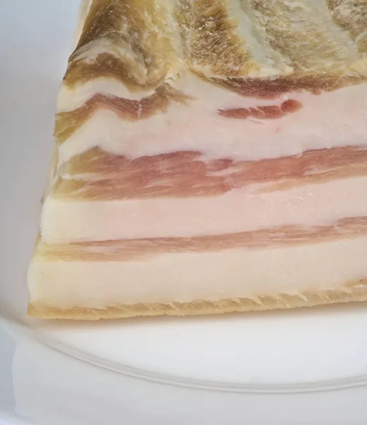 En bit bacon med ett lager rött på en vit närbild platta. — Stockfoto