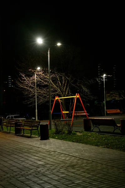 Metrópole noturna à noite. Pólos de iluminação da cidade são iluminados e um parque infantil é visível. — Fotografia de Stock