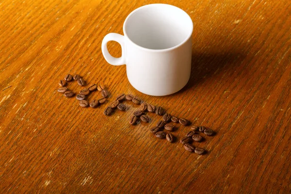 Lettering chicco di caffè e una tazza bianca su uno sfondo di legno. — Foto Stock