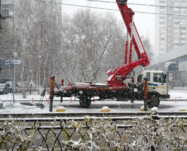 MOSKAU, RUSSLAND - 22. November 2021: Der Kran steht zusammen mit der Maschine auf Stützen auf der Straße und hebt etwas. Schnee fällt — Stockfoto