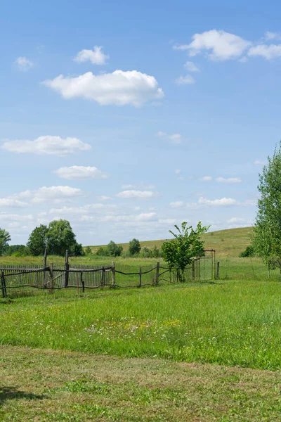 Sommarlandskap i utkanten av Ryssland. Blå himmel och vita moln. Det finns en hel del grönt gräs och en by staket är synlig. — Stockfoto