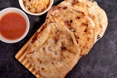 Pupusas 'ı tahta bir tahtada siyah mermer arka planda el yazısı ve sos ile kapatın.