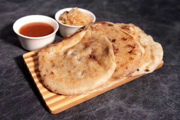 Ahşap bir tahtanın üzerinde siyah mermer bir arka planda el yazısı ve sos olan köpek yavruları.