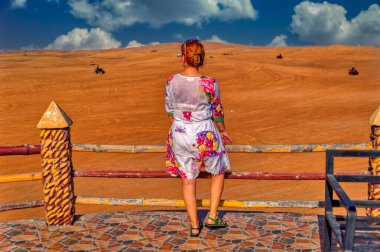 Bir kadın terasta duruyor ve Dubai çölüne bakıyor..