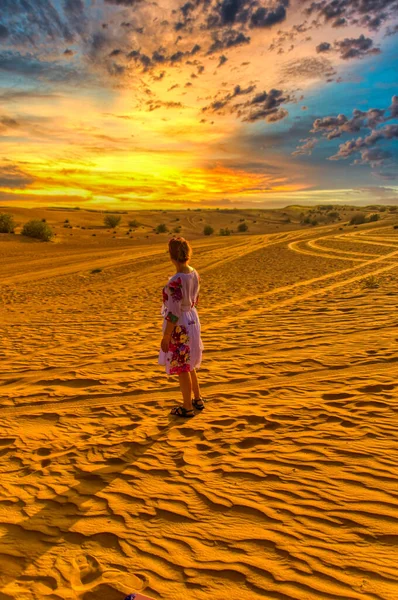 Bir kadın çölde duruyor ve gün batımını seyrediyor..