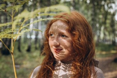 Kızıl saçlı bir kızın yüzünde, Sonbahar yapraklarının gölgesi güneşte