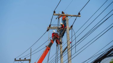 Elektrikçiler kablo ve ekipman yüklemek için yüksek voltaj kuleleri üzerinde çalışıyorlar.