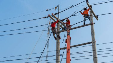 Elektrikçiler kablo ve ekipman yüklemek için yüksek voltaj kuleleri üzerinde çalışıyorlar.