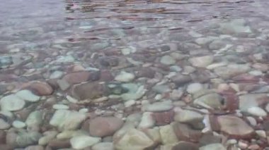 Pembe deniz taşları üzerinde şeffaf deniz dalgaları parıldıyor. Deniz sahnesi. Sudaki taşlar