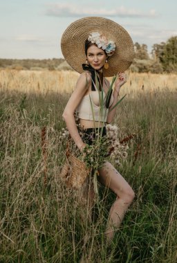 Üstü ve şortlu, şapkalı ve çiçekli kızlar, doğanın arka planına karşı poz veriyorlar. İlk kız sazlığın sapını tutuyor. Elinde sepet olan başka bir kız....
