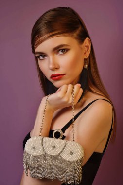 A young beautiful girl posing in a black leather jacket and gold jewelry on a background in a photo studio.