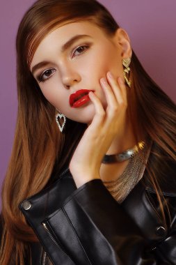 A young beautiful girl posing in a black leather jacket and gold jewelry on a background in a photo studio.