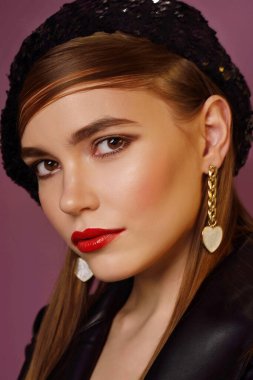 A young beautiful girl posing in a black leather jacket and gold jewelry on a background in a photo studio.