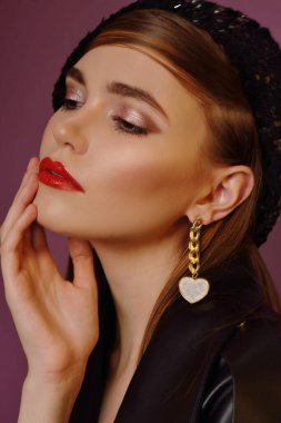 A young beautiful girl posing in a black leather jacket and gold jewelry on a background in a photo studio.