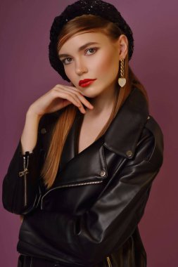 A young beautiful girl posing in a black leather jacket and gold jewelry on a background in a photo studio.