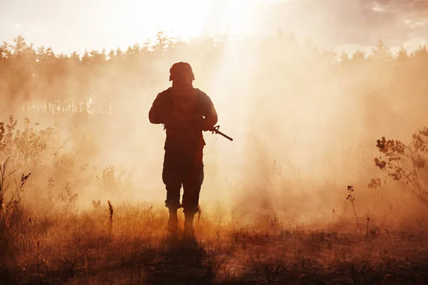 soldier in fog. Military silhouette, army helmet, warpaint, smoked dirty face, tactical gloves. Military action, desert battlefield, smoke grenades