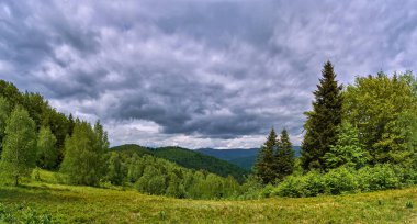 Bulutlu bir günde yaz dağı manzarası. Yeşil, yağmur öncesi orman tepeleri. Yaz yeşillikleri bir sağanağın nemini dört gözle bekliyor.