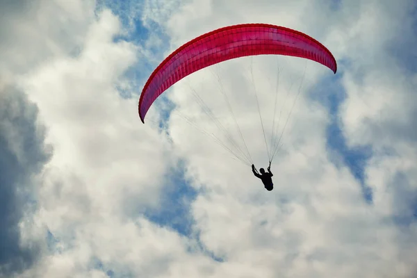 Paraglider uçuyor. Bulutlu gökyüzünde kırmızı paraglider