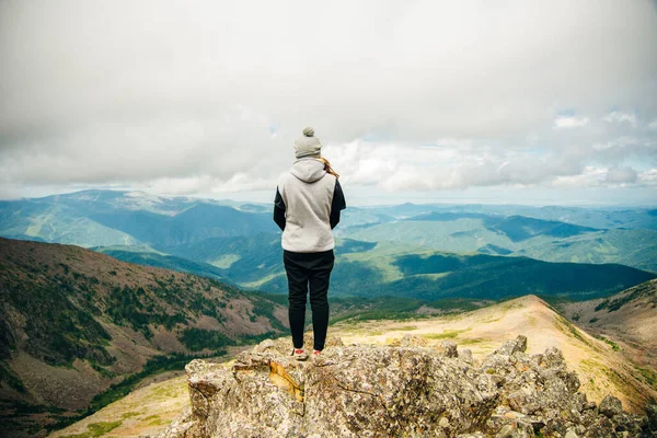 一个穿着暖和衣服的女孩背靠在山顶站着 上面有美丽的高山和湖泊 高质量的照片 — 图库照片