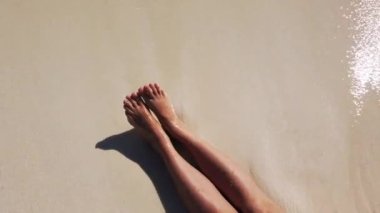 Kumsalda kumların ve dalgaların arkasında bronzlaşmış dişi bacaklar. Yüksek kalite 4k görüntü