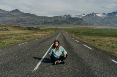 Kız, İzlanda manzaralarının arka planında yolda oturuyor. Yüksek kalite fotoğraf