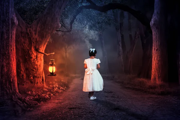 A little girl walks on the path at night, where the light from the lanterns slowly illuminates the path alone.