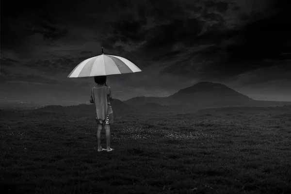 A black-and-white picture of a young girl standing with an umbrella and watching a terrifying rainstorm form.