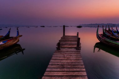 Gondora teknesi. Tahta köprü ve balıkçı ahşap bir tekne güneş doğarken U-Bein Köprüsü 'nün altına park edilmiş. Amarapura, Mandalay, Mynmar.