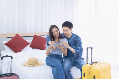 Tatil planı yap. Sevgili çift yatak odasında tablet ve rezervasyon bilgilerini arıyor..