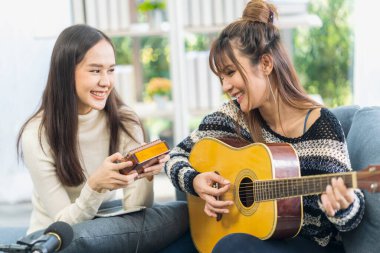 Oturma odasında gitar çalan iki genç kadın..