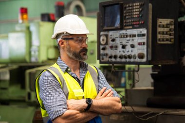 Üretimdeki yakışıklı teknisyen. Kafkasyalı orta yaşlı mühendis üniformalı fabrikada üretim kalitesini kontrol ediyor..