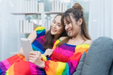 Lgbt Kavramı. Gökkuşağı elbiseli iki genç kadın oturma odasındaki kanepede tablet kullanıyor..