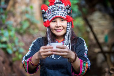 Tepe kabilesi elbiseli bir kadın elinde bir fincan kahve tutuyor. Sıcak kahve fincanı olan genç Asyalı kadın..