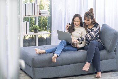 Oturma odasında dizüstü bilgisayar kullanan kadın çiftler. Genç ve çekici bir kadın dizüstü bilgisayar kullanıyor. Evdeki kanepede oturuyor. Kanepede dinleniyor..